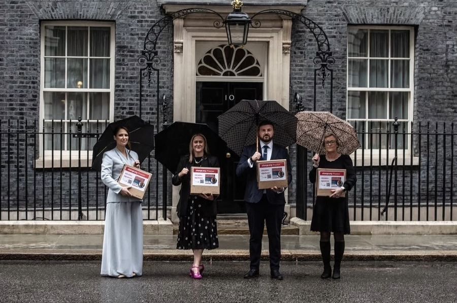 Four campaigners holding petition boxes outside the door of 10 Downing Street in the rain.