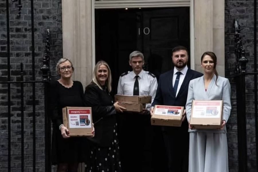 Campaigners and a police officer holding the petition boxes at the door of 10 Downing Street.