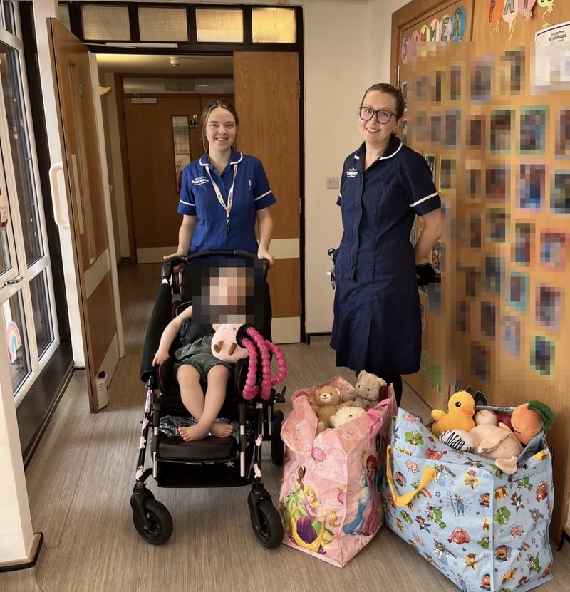 Two nurses at Brian House Children's Hospice with bags of teddy bears from Preston's vigil. A child's face is blurred.