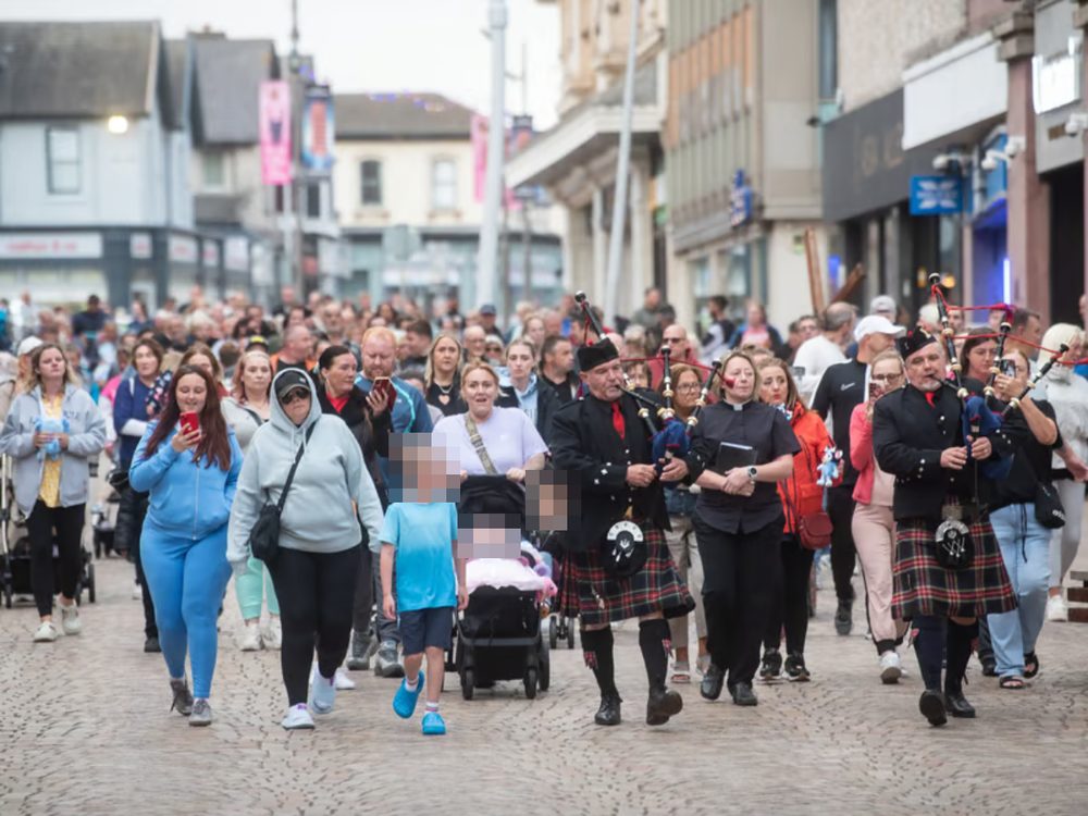A large crowd walking through Blackpool town centre for Preston's vigil, led by two pipers.